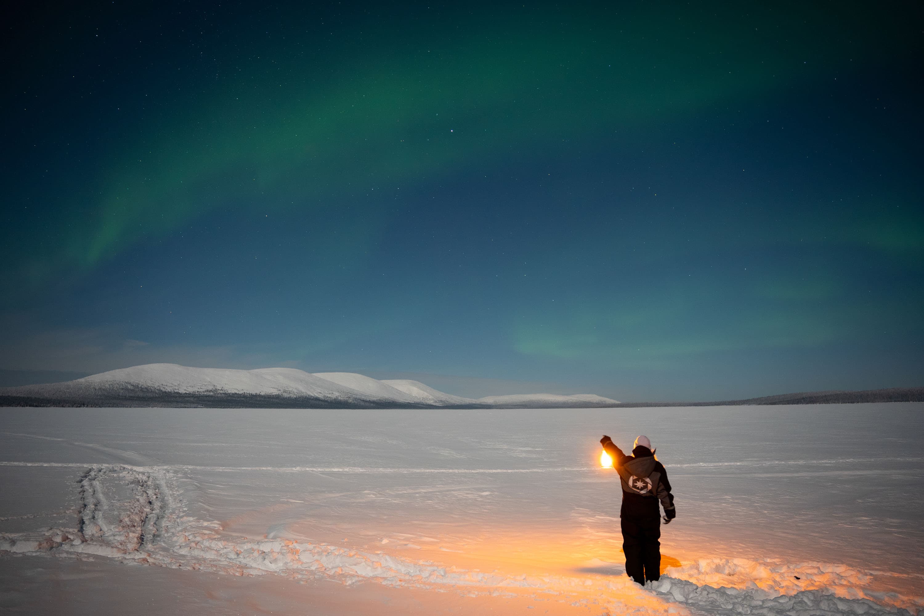 Aurora borealis over snow-covered Arctic landscape with a person holding a light near the foreground