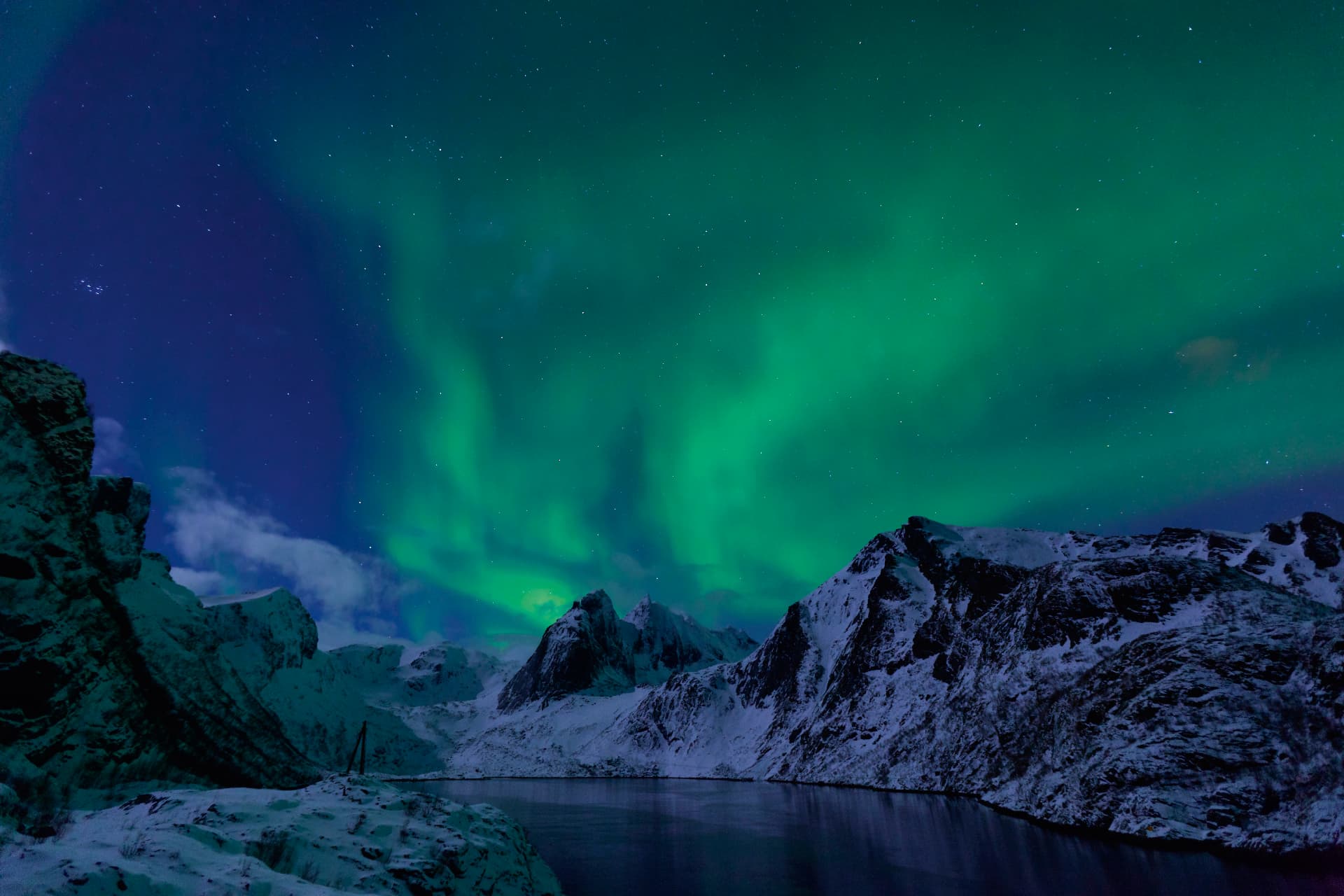 Northern lights glowing green over snow-covered fjord mountains