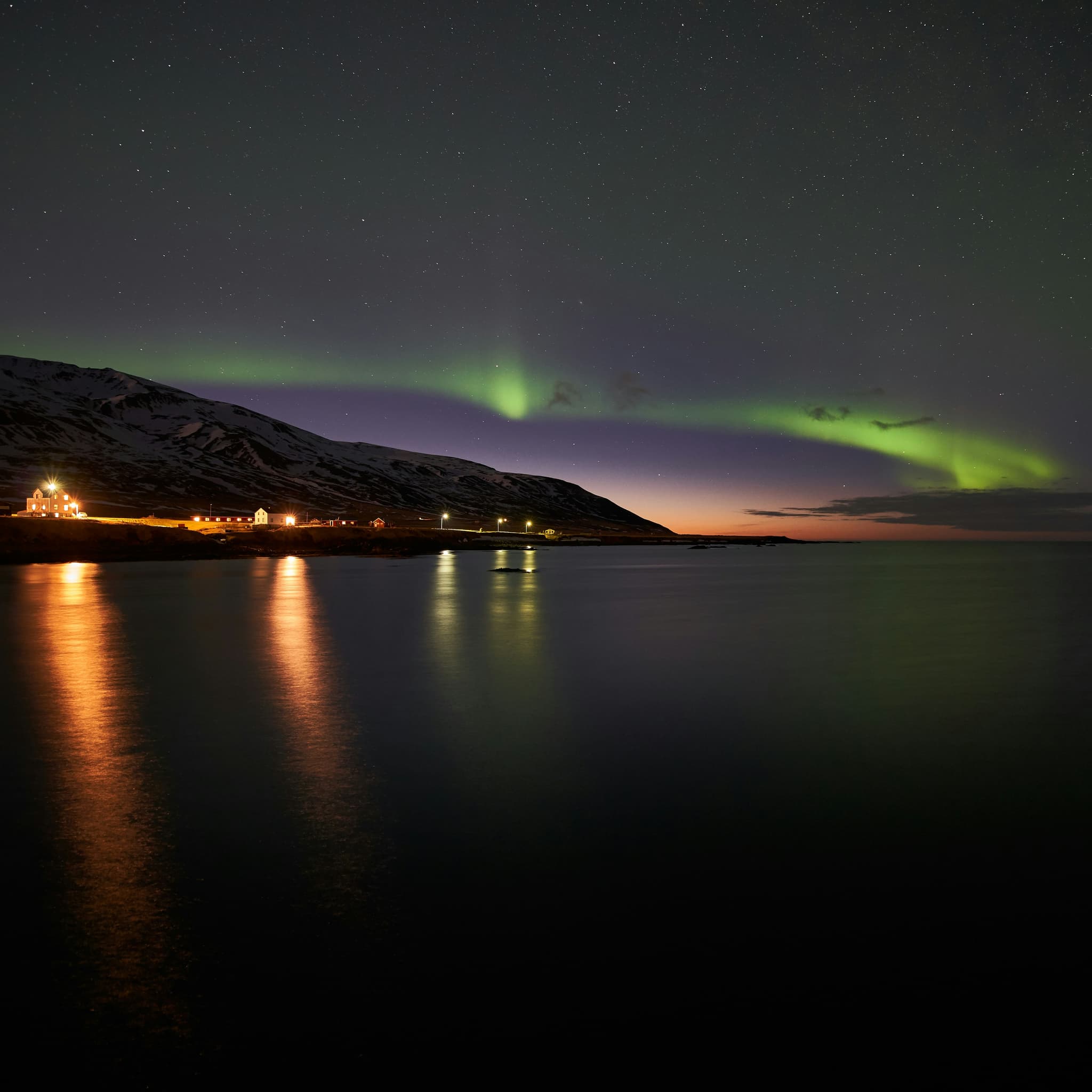 Northern lights over a snowy mountain coastline