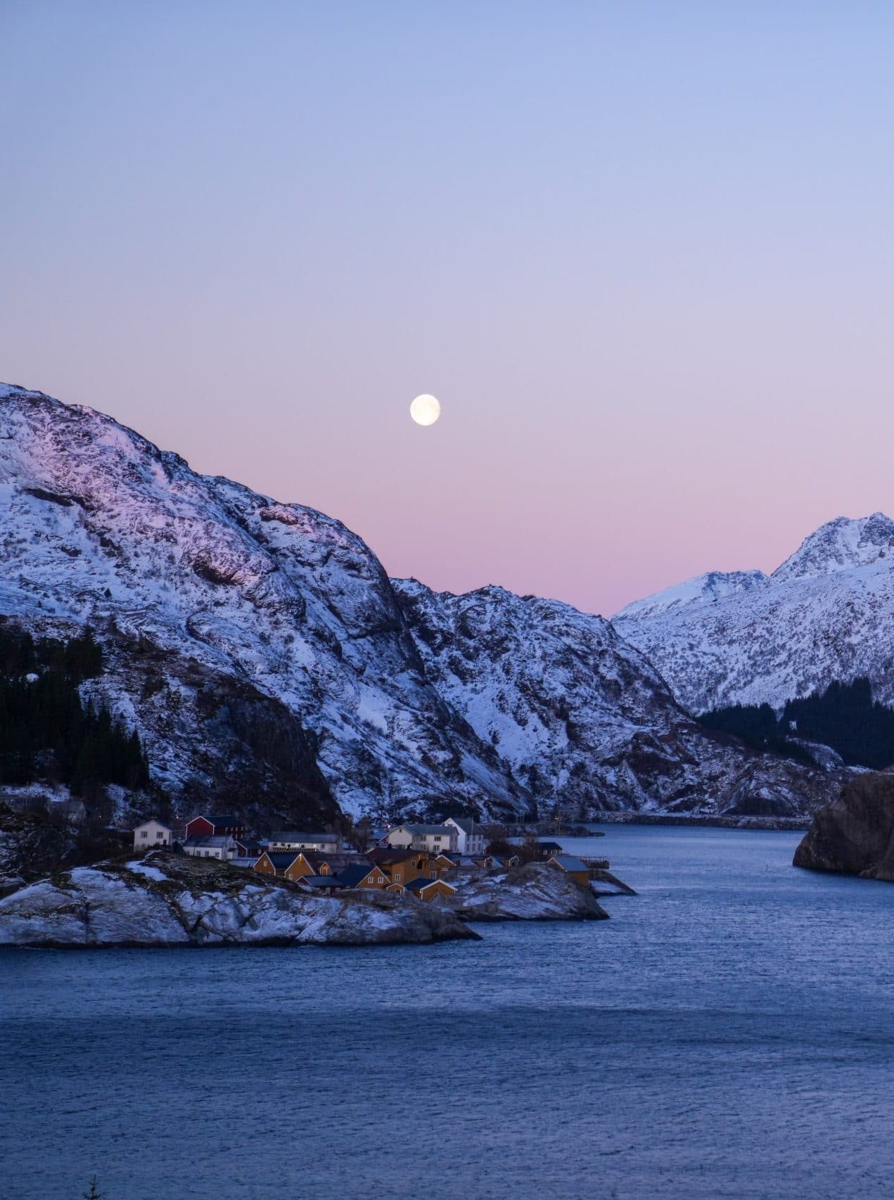 Winter coastal village at dusk beneath snow-covered mountains