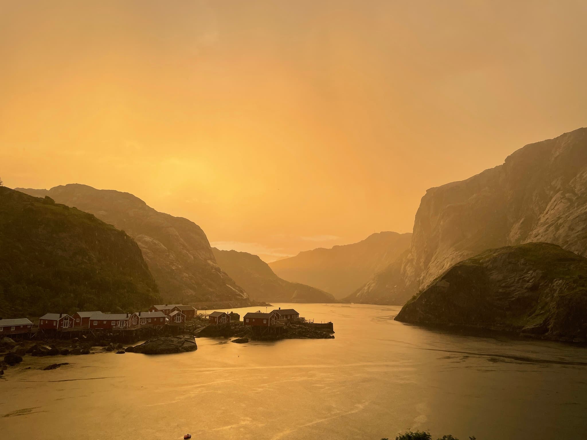 Waterfront cabins on a Lofoten fjord beneath dark mountains at golden hour