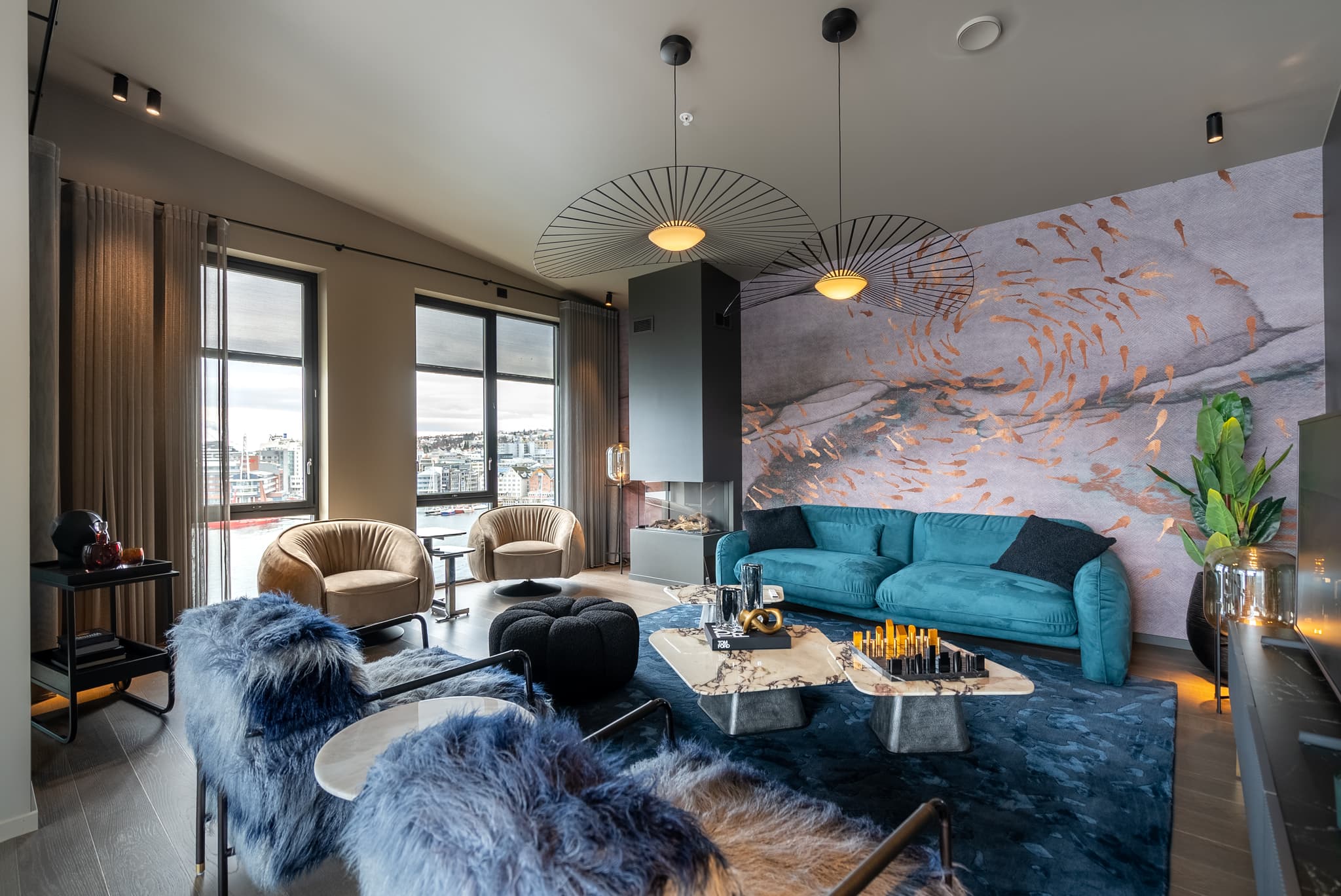 A modern lounge with teal and beige seating, sculptural pendant lights, large windows, and a city view.