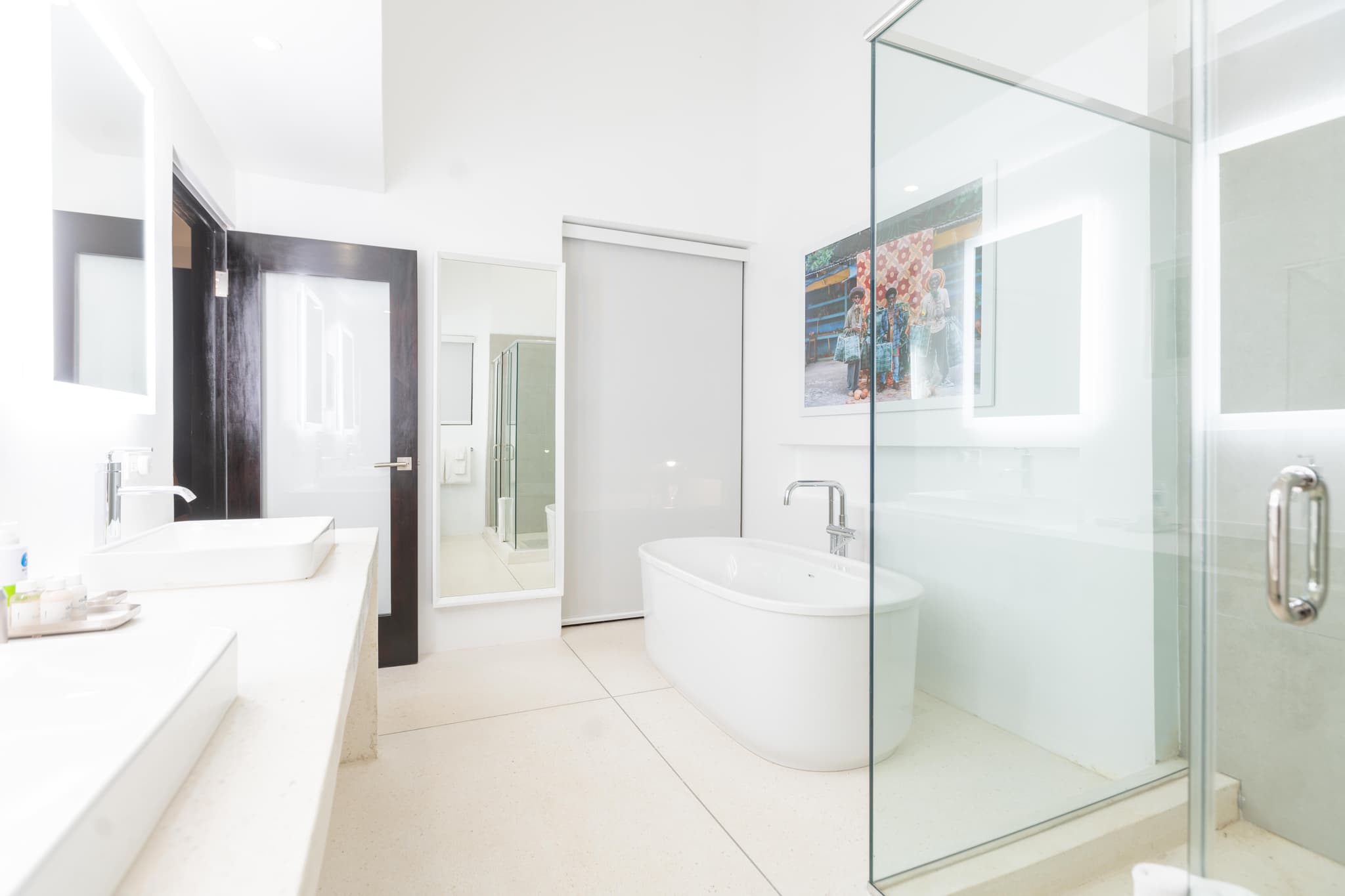 A bright modern bathroom with a freestanding bathtub, glass shower enclosure, double sinks, and a wall mirror.
