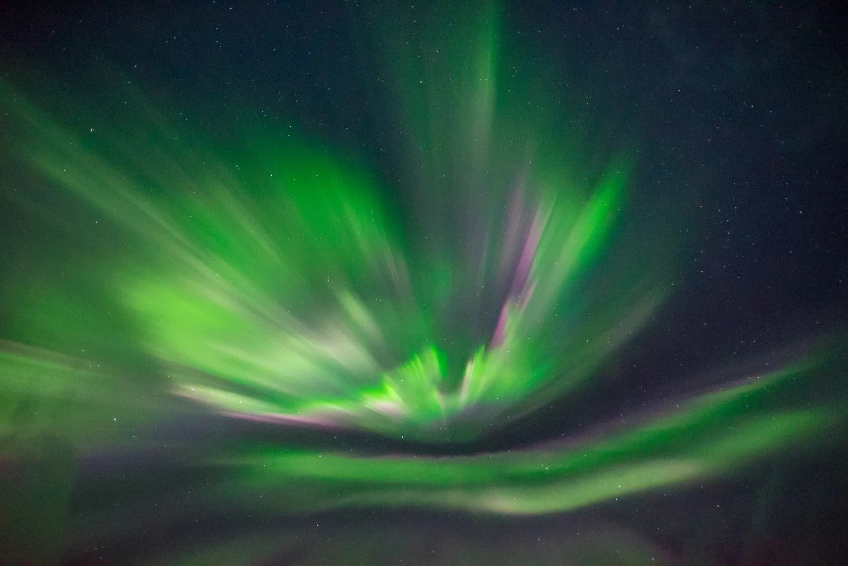Bright green and purple northern lights streak across a starry night sky.