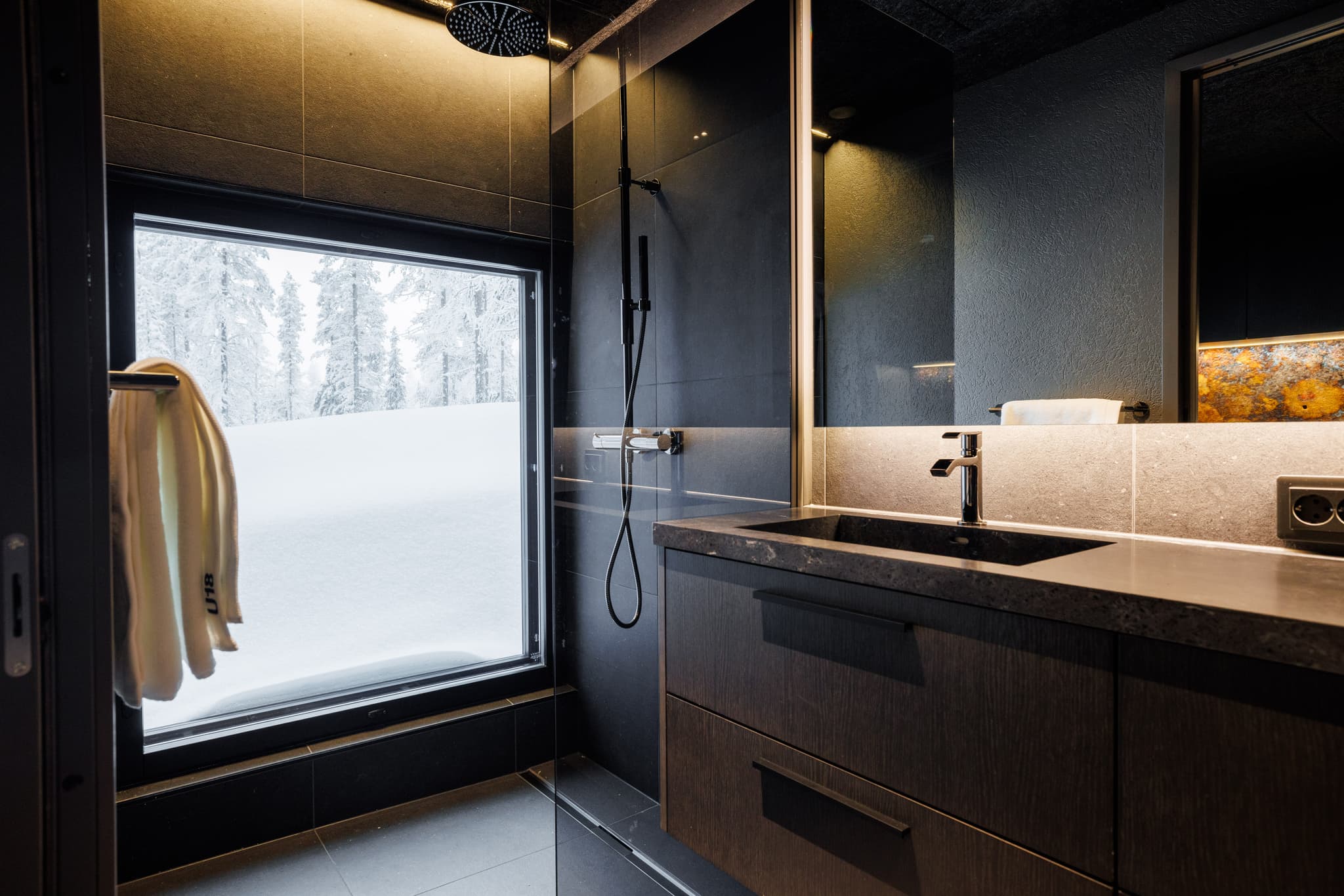 Luxury bathroom interior with glass shower, stone sink vanity, and winter snow visible through the window.