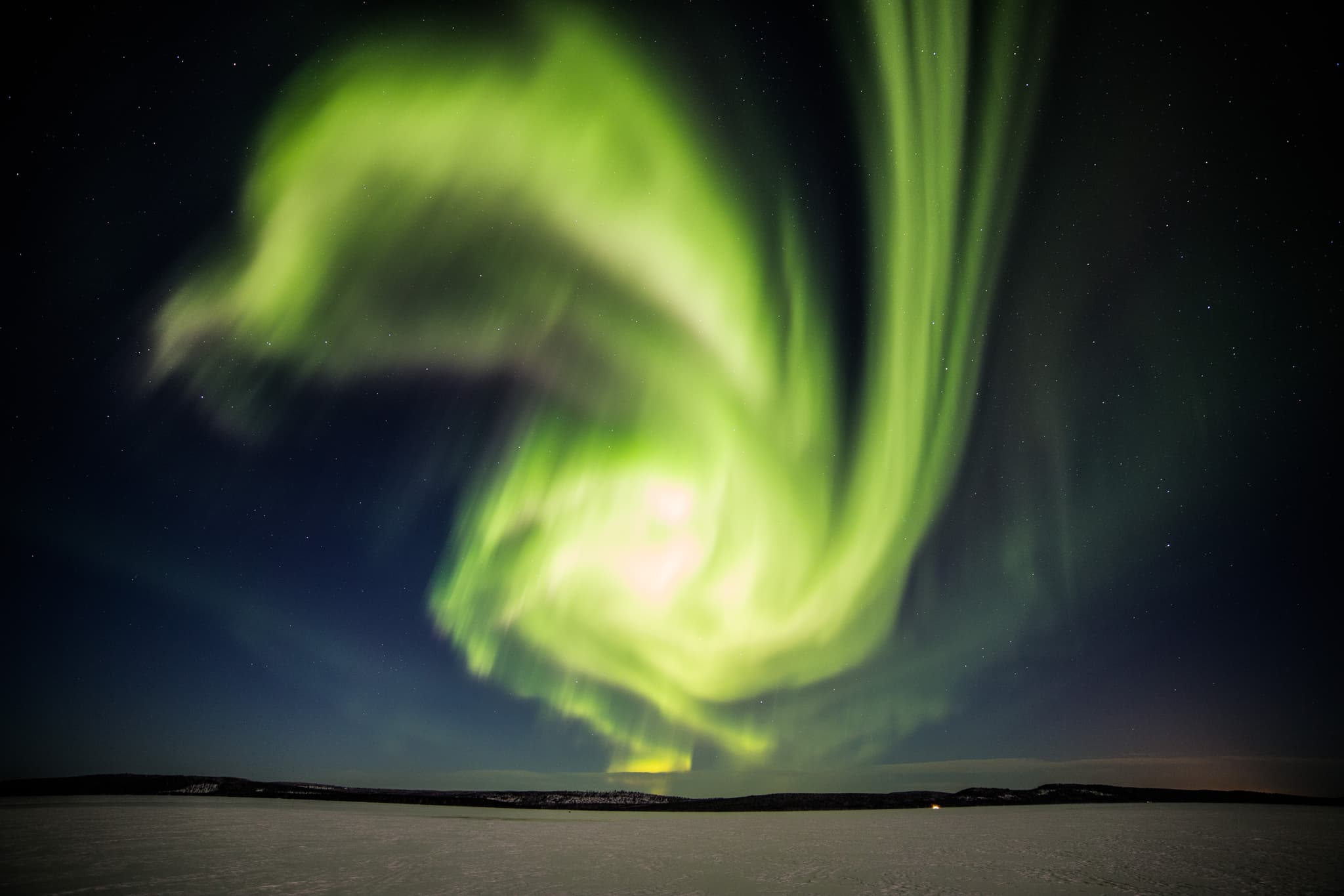 A vivid green aurora swirls across a starry night sky above a snowy landscape.