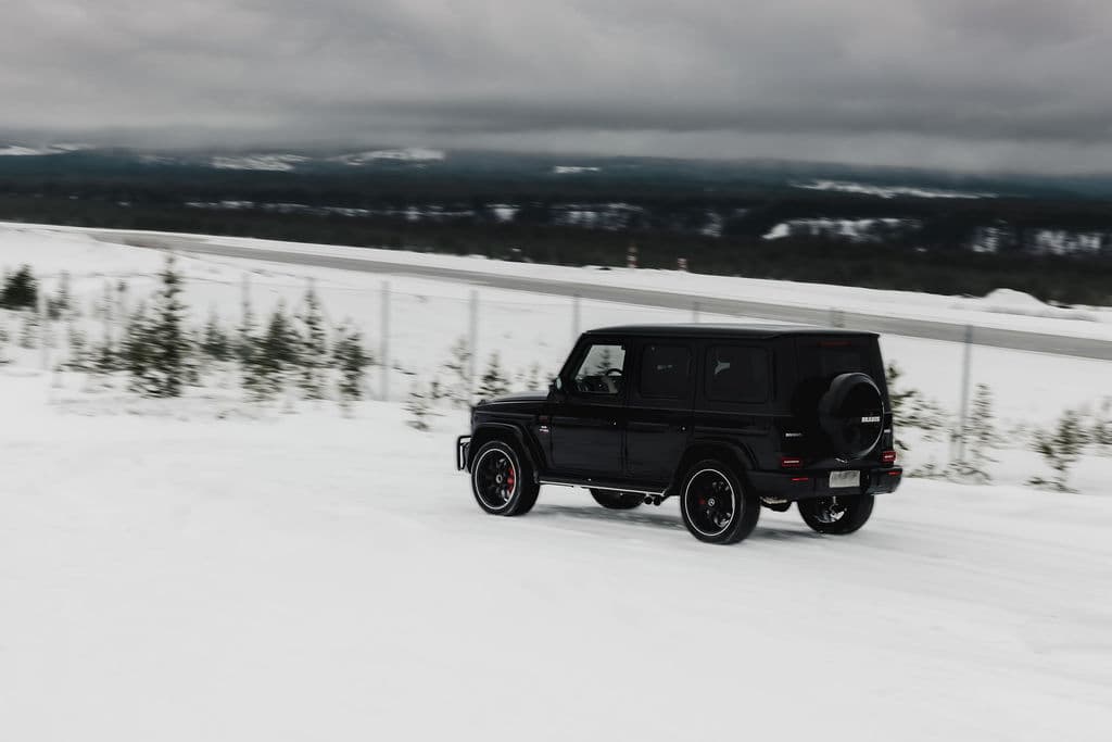 A black SUV drives across a snowy landscape under a cloudy winter sky.