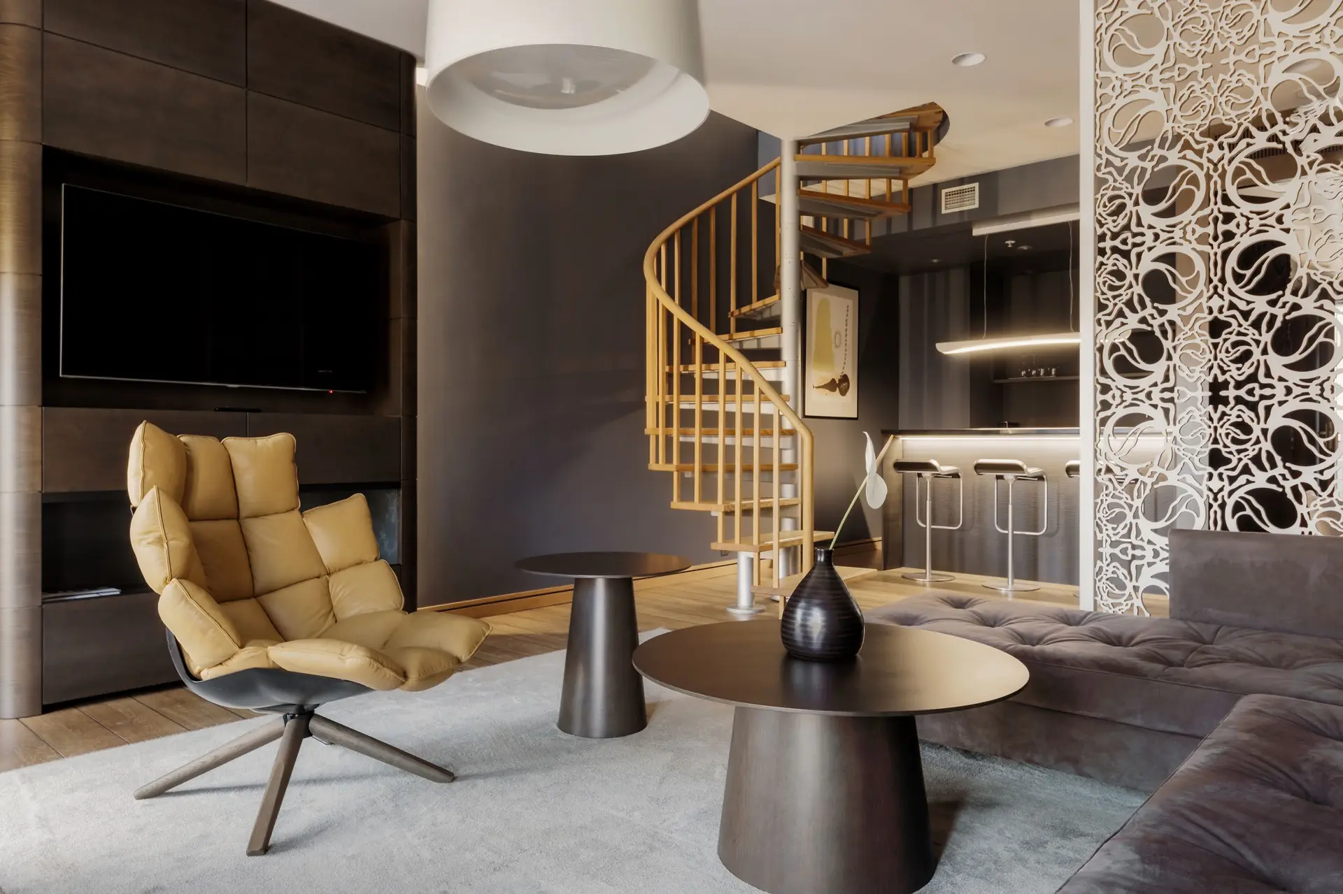 A modern luxury penthouse living area features a spiral staircase, lounge chair, sectional sofa, and bar nook.