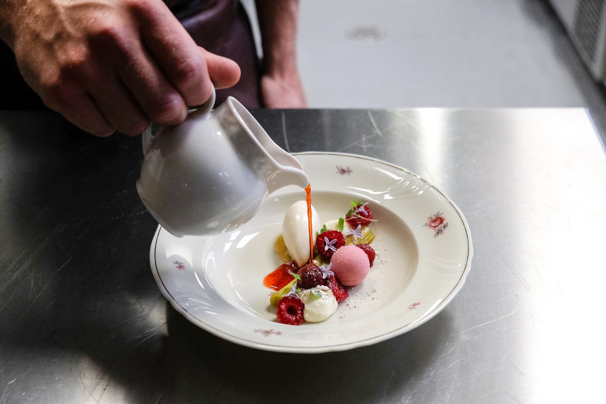 Chef pouring sauce onto a plated dessert with berries and colorful garnishes