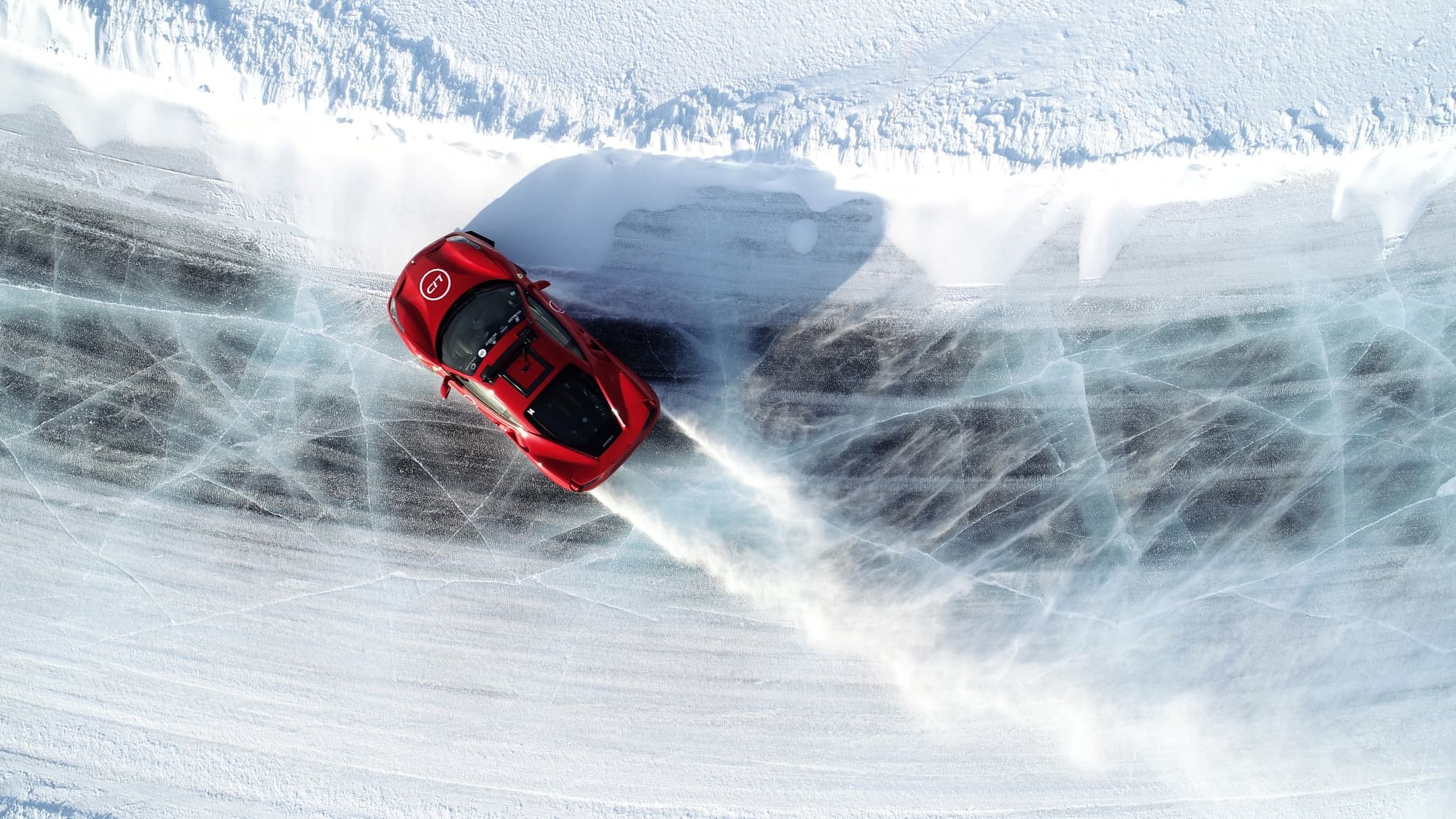 A red sports car drifts across a frozen icy surface, leaving a spray of snow and ice behind it.