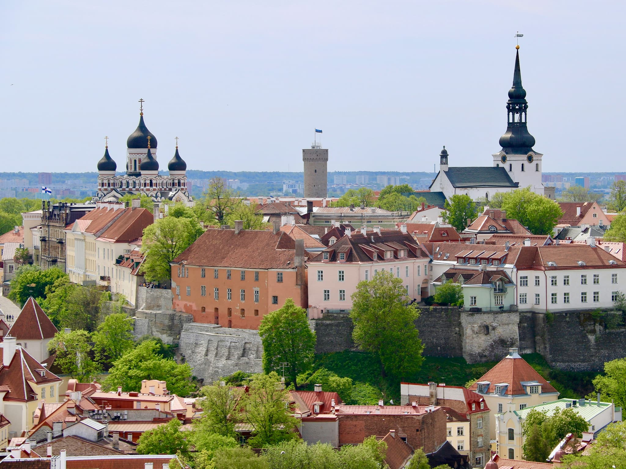 A panoramic view of a historic old town with red-roofed buildings, stone walls, and several church towers rising above the city skyline.