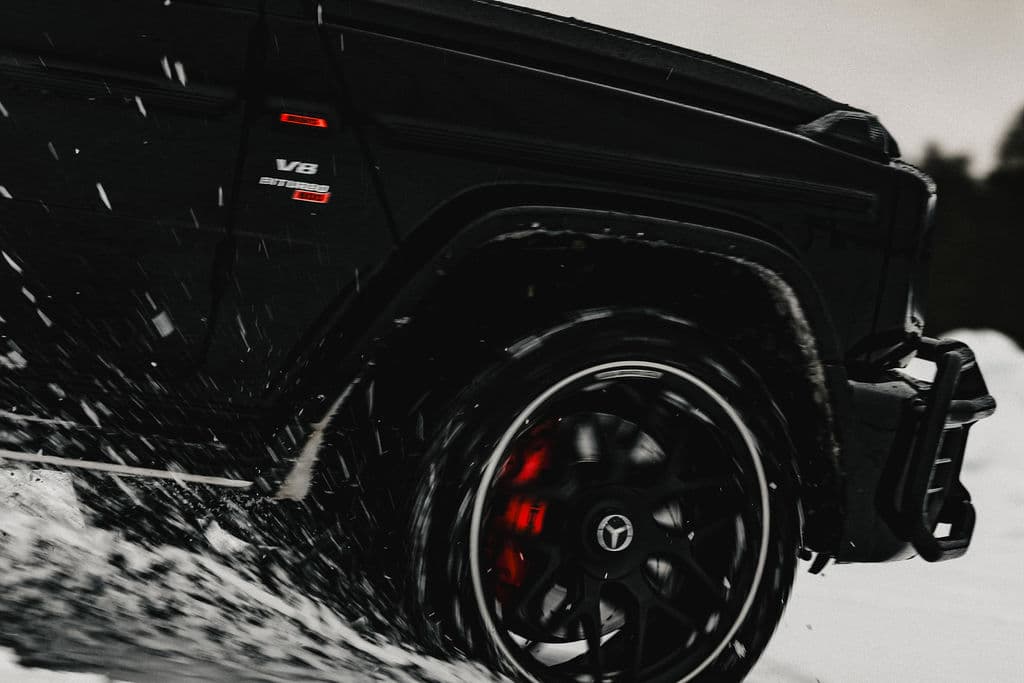 A black SUV drives through snow, with the front wheel kicking up spray and slush.