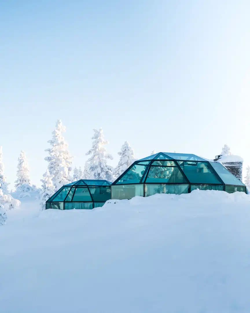 Two glass igloo-style cabins sit in deep snow among frost-covered trees under a pale winter sky.