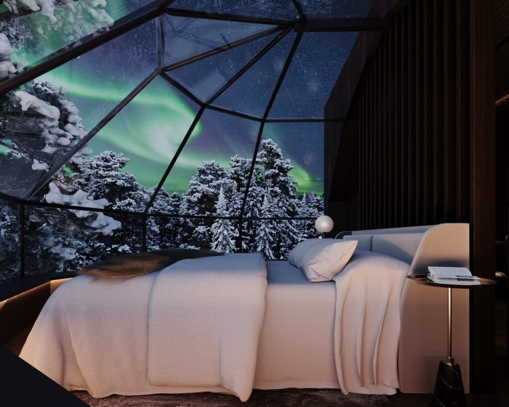 A cozy bed sits inside a glass-domed bedroom with snowy trees and green aurora visible outside at night.