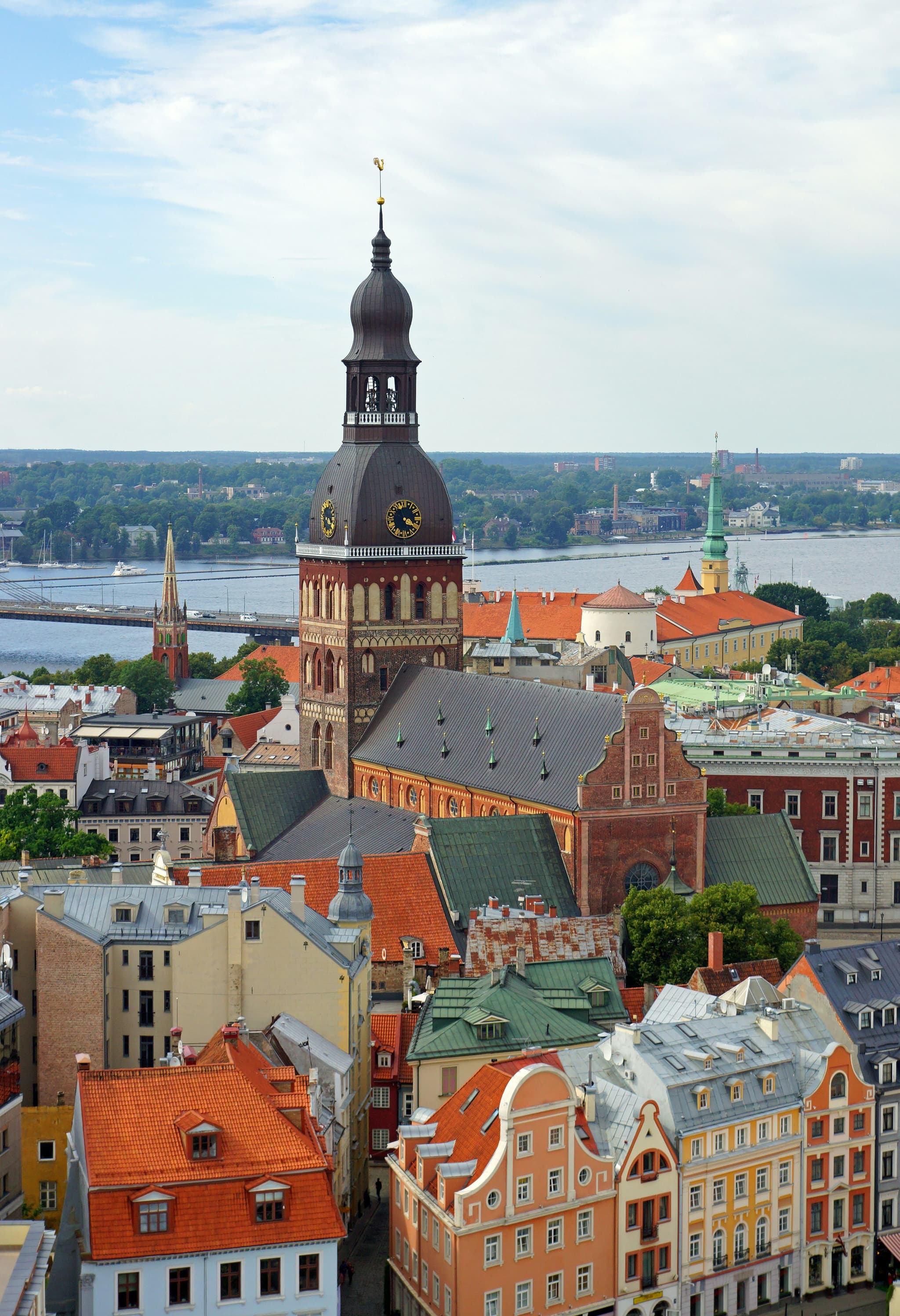 A high-angle view shows a historic city center with colorful rooftops, a tall church tower, and a river in the background.