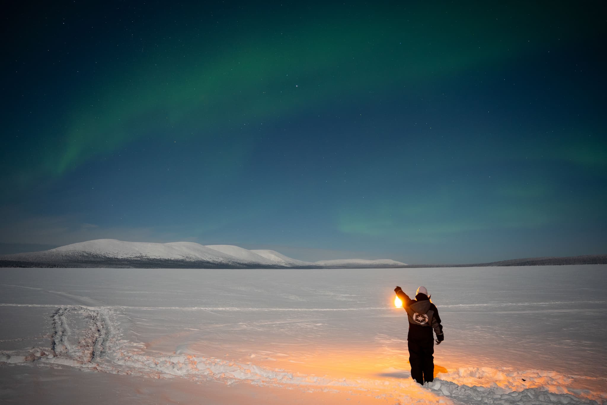 Aurora borealis over snow-covered Arctic landscape with a person holding a light near the foreground