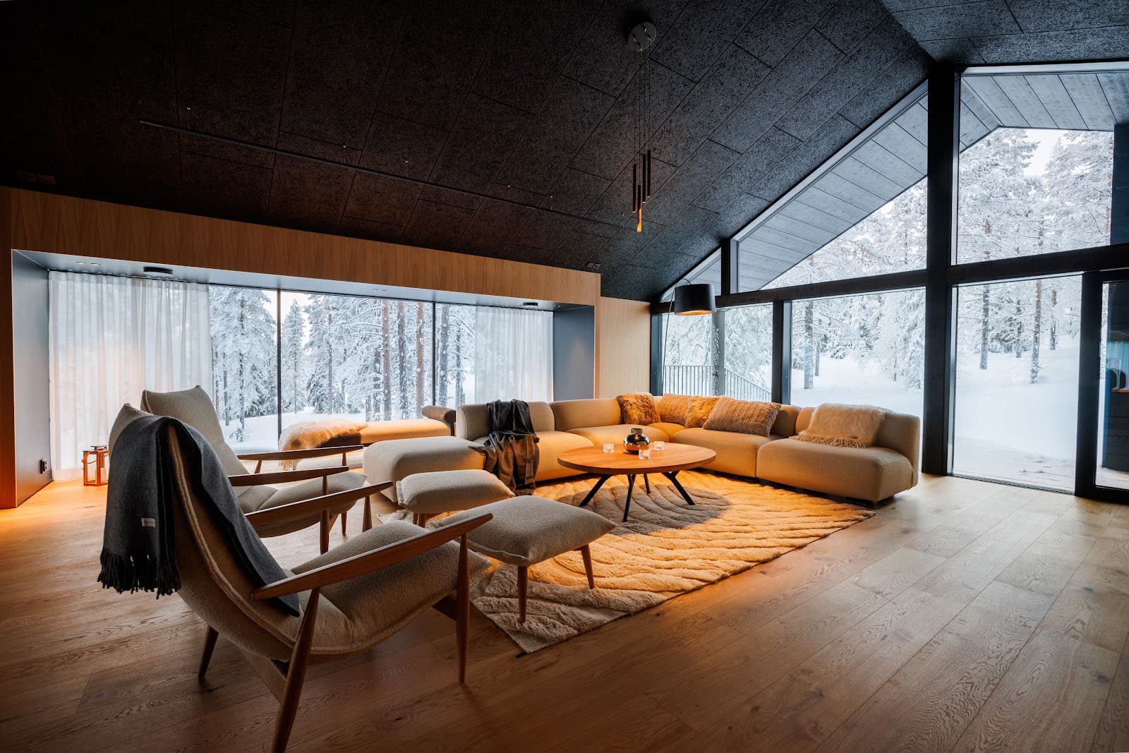 Luxury living room with large windows showing a snowy forest, a beige sectional sofa, and cozy throws and cushions.
